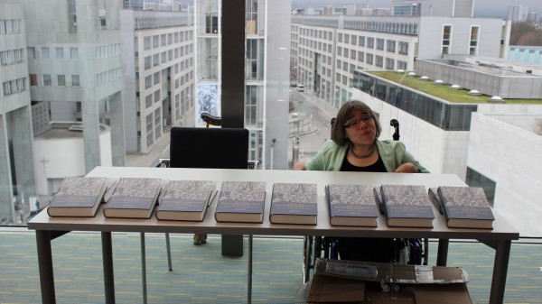 Sandra Hermann sitzt an einem Tisch mit Büchern von Andreas Nastl